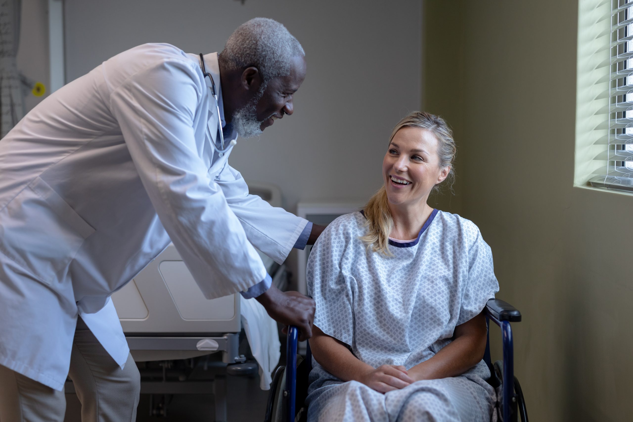 Diverse male doctor and female patient sitting on wheelchair smiling to each other. medicine, health and healthcare services.